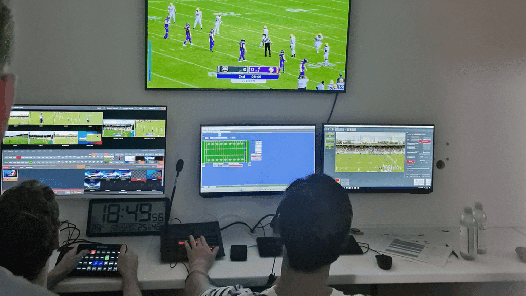 Two men seated at a desk with several monitors, operating a live stream with VIZRT character generator software